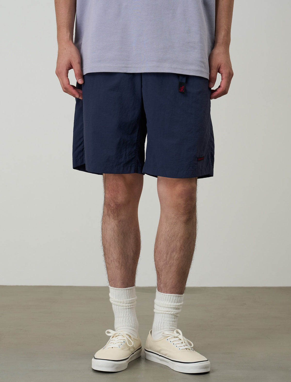 Person wearing navy shorts, white socks, and white sneakers on a plain background