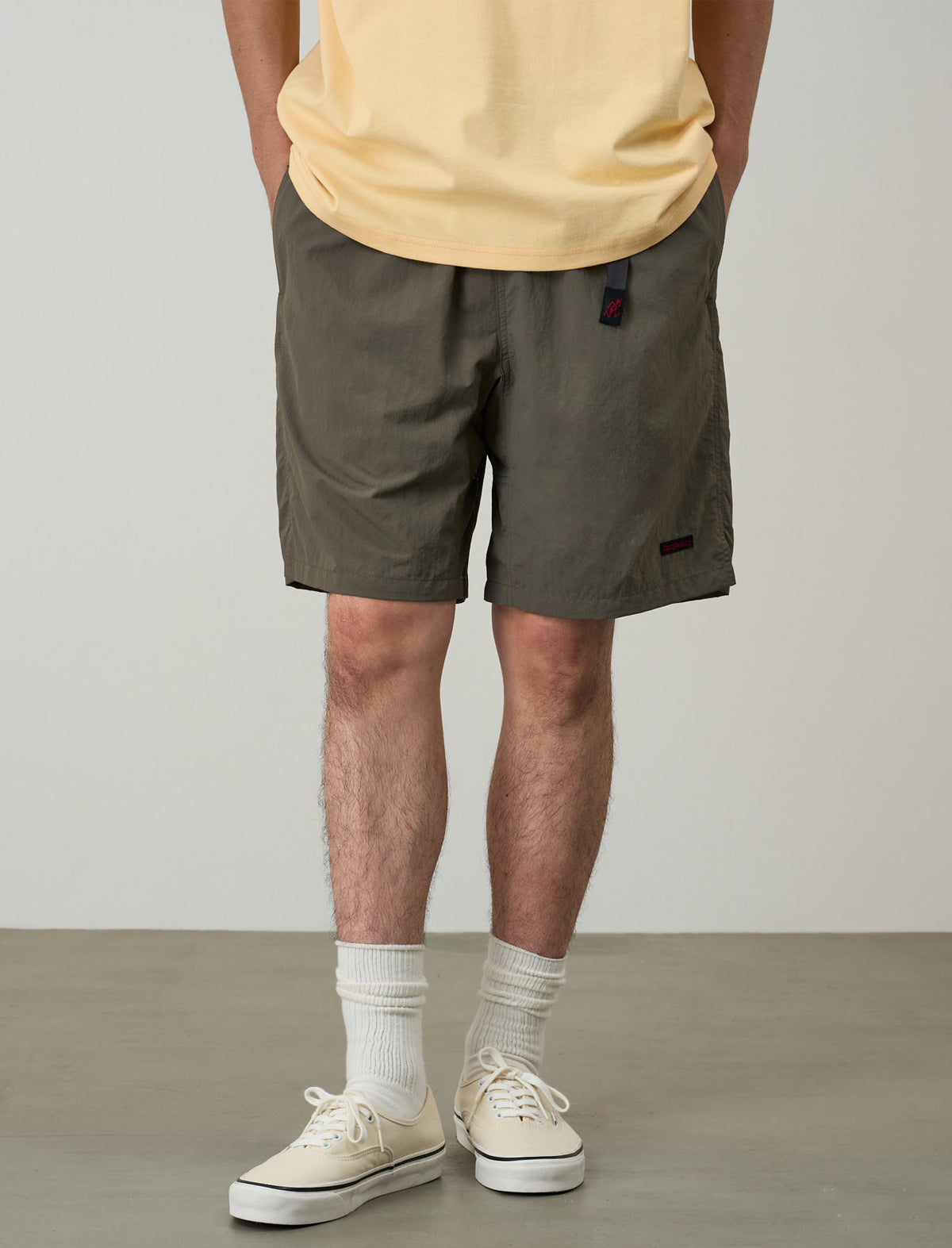 Person wearing olive green shorts, yellow shirt, white socks, and white sneakers on a plain background