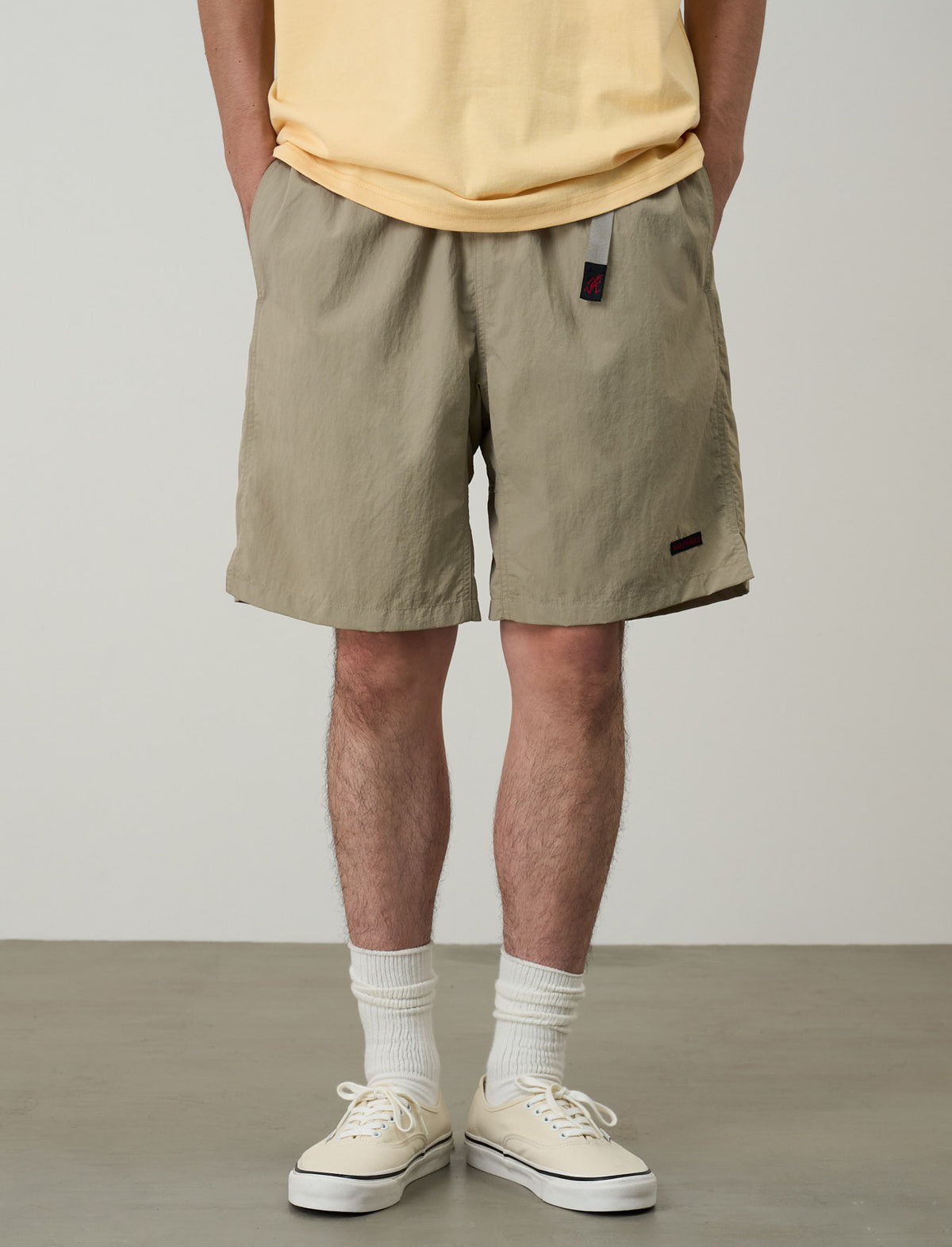 Person wearing beige shorts and white sneakers on a plain background