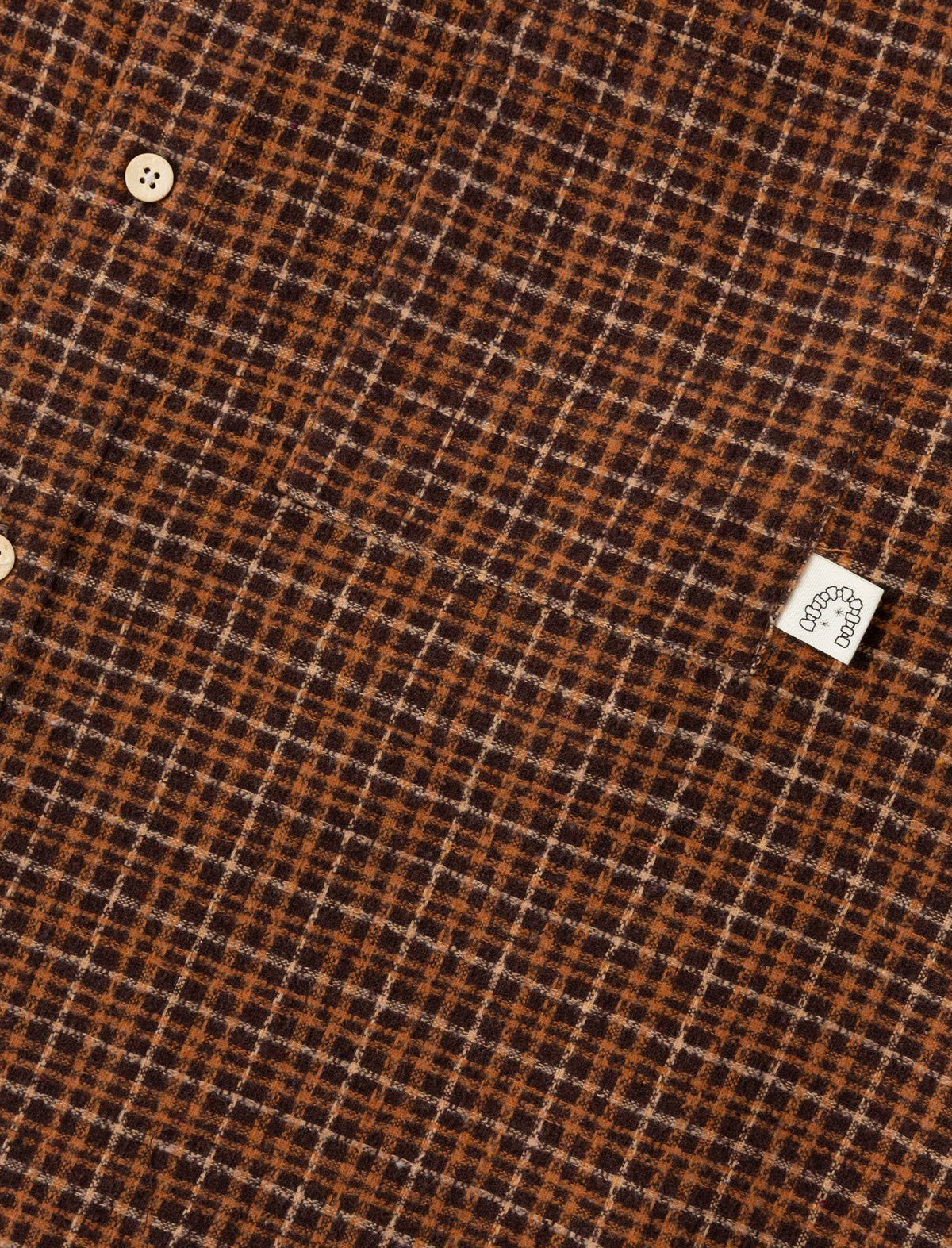 Close-up of Heresy Deft brown and black checkered fabric with a brand label.