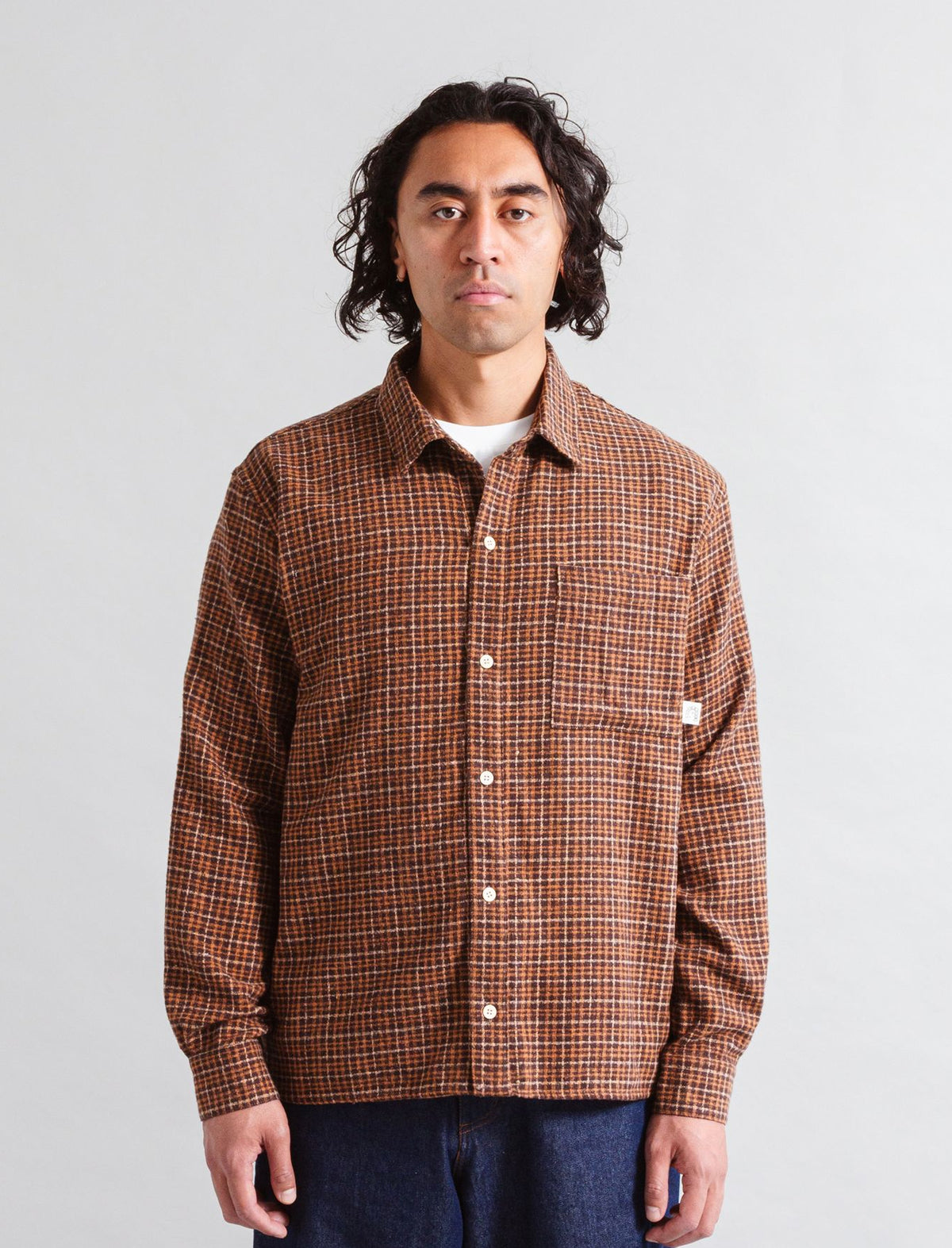 Man wearing a Heresy Deft brown plaid shirt against a plain background