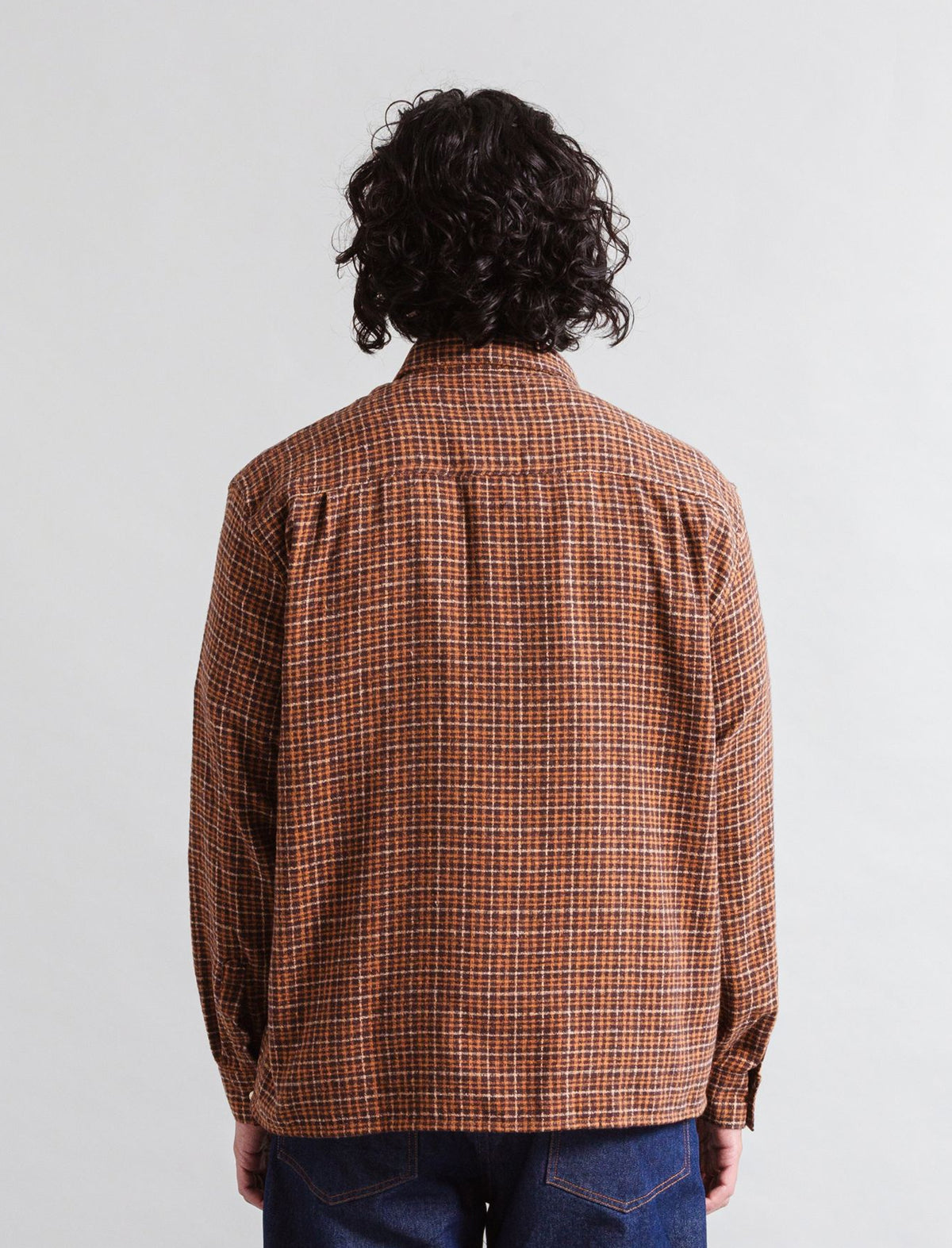 Person wearing a Heresy Deft brown plaid shirt from behind on a white background