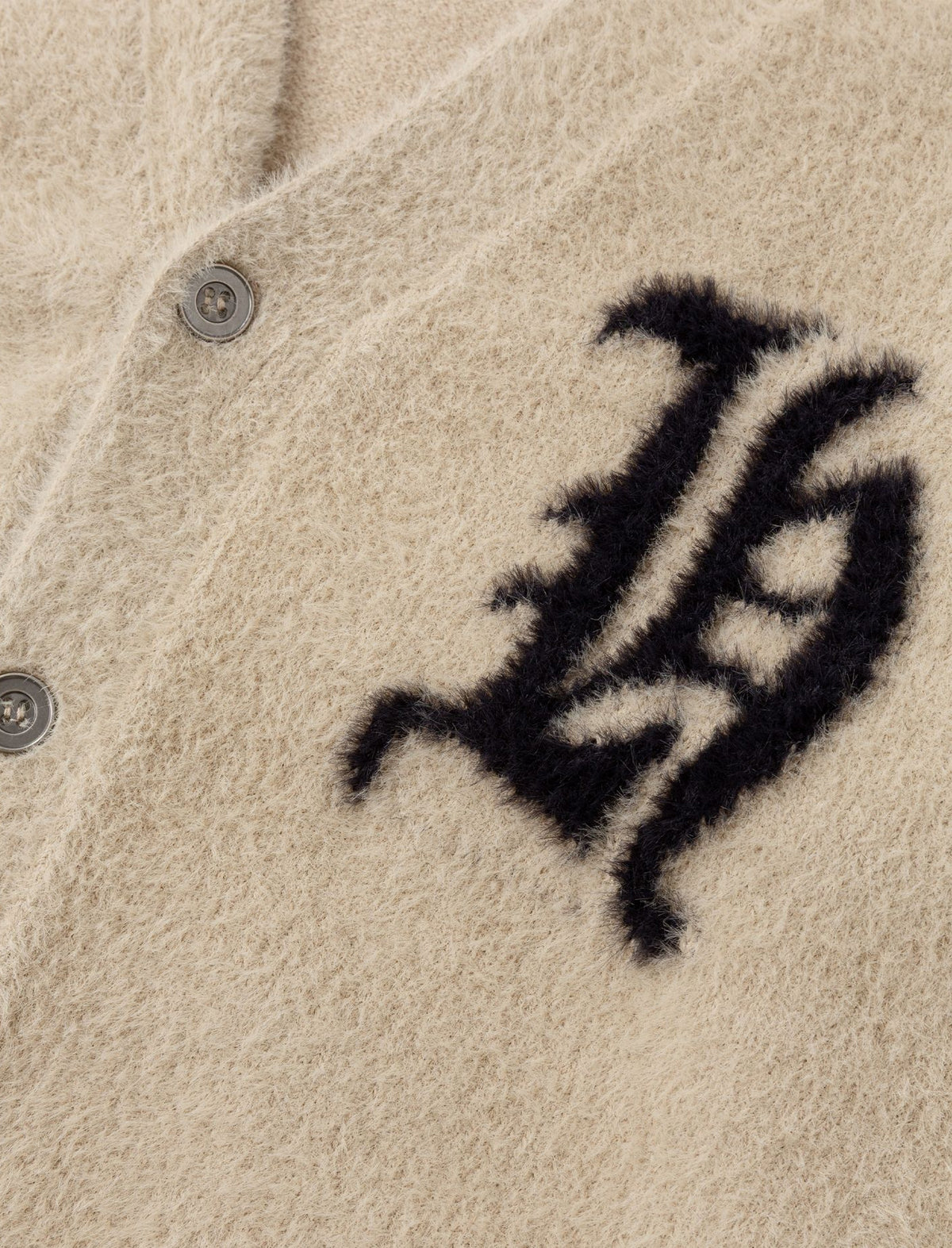 Heresy 'H' cardigan close-up of a textured beige fabric with a black logo on a button.