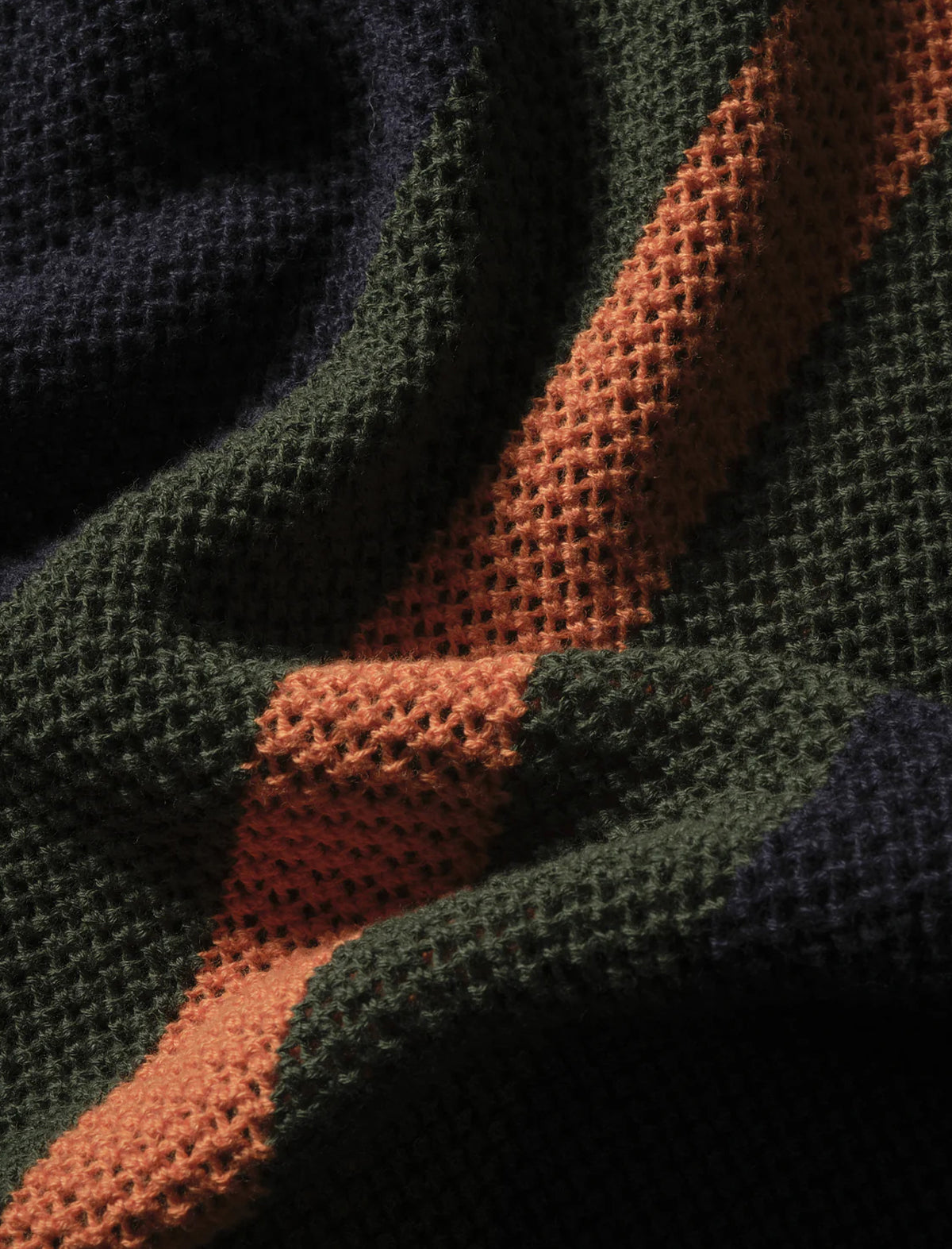 Close-up of a textured fabric with wavy pattern in green, orange, and black.