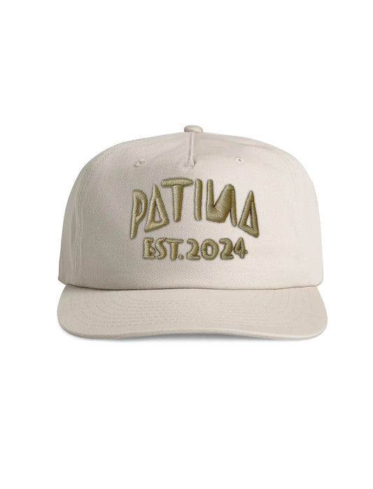 A beige baseball cap with 'PATINA EST. 2024' embroidered on the front in a metallic gold tone, shown against a plain white background.