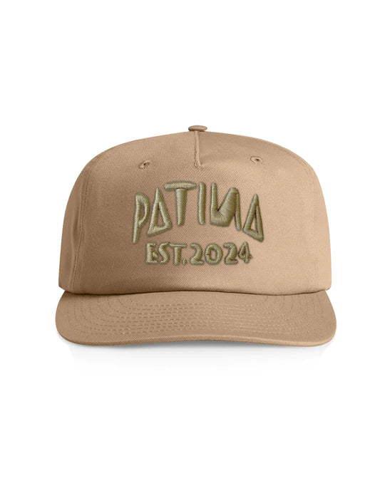 A tan baseball cap with 'PATINA EST. 2024' embroidered on the front in olive green, shown against a plain white background.
