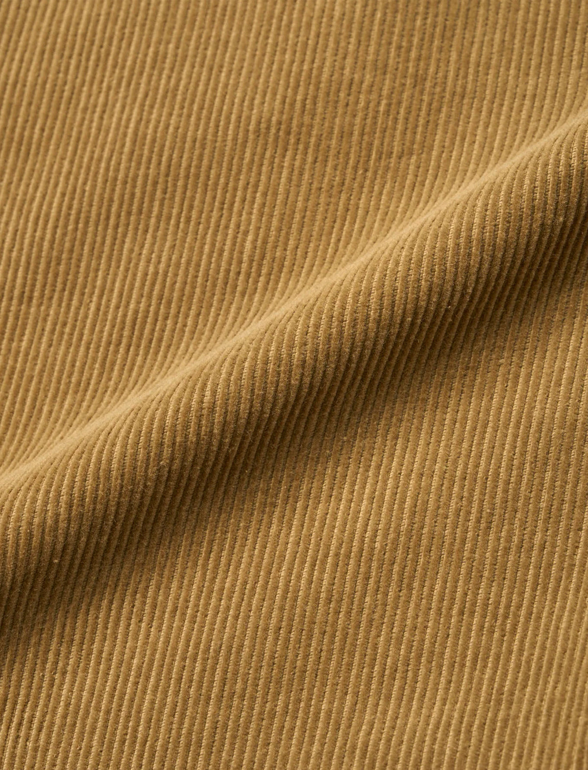 A close-up of a ribbed fabric texture in a warm camel brown color, showing the fine vertical corduroy-like ridges and a soft diagonal fold.