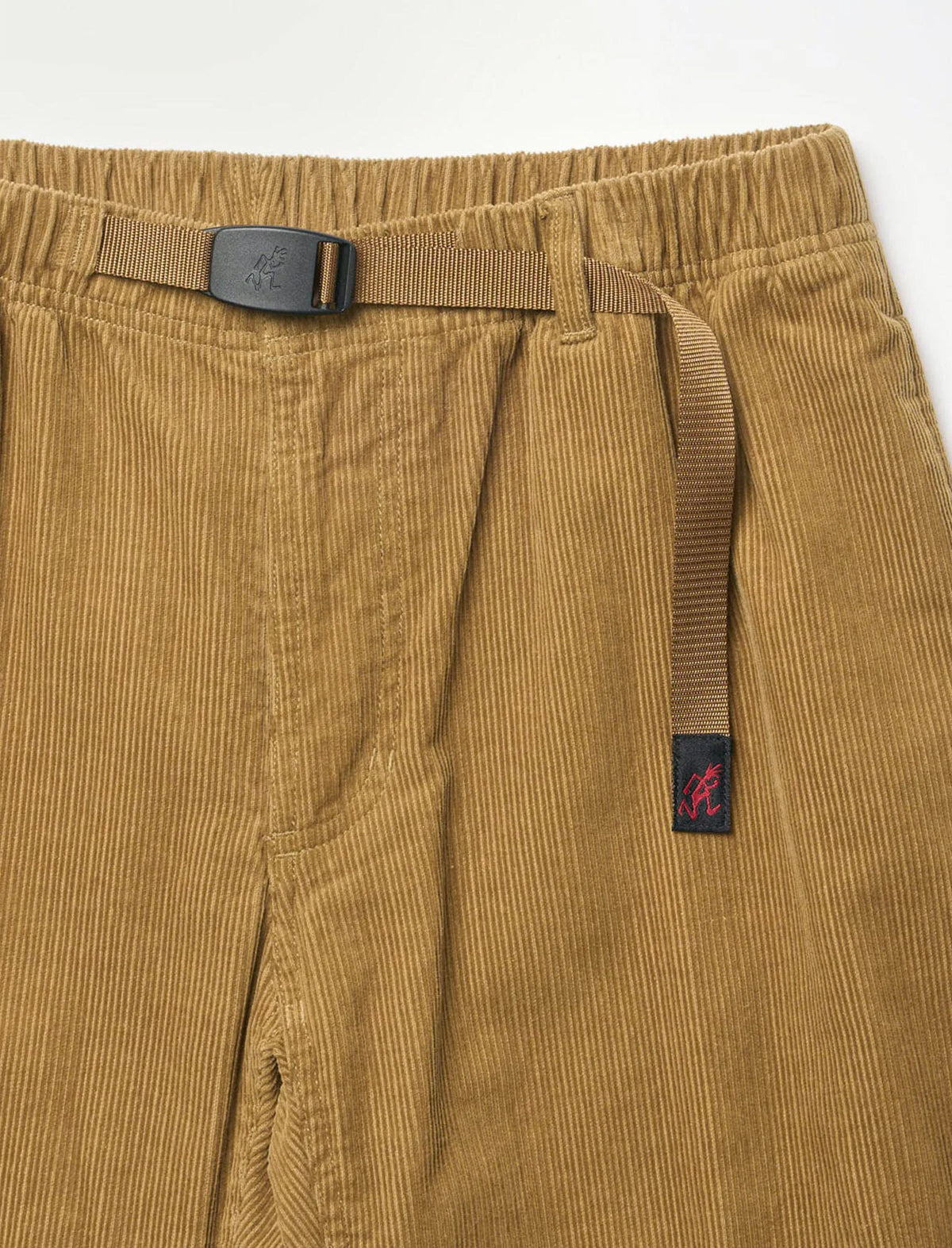 Close-up of tan corduroy pants with a matching belt and a small embroidered logo patch on the side, photographed against a plain white background.