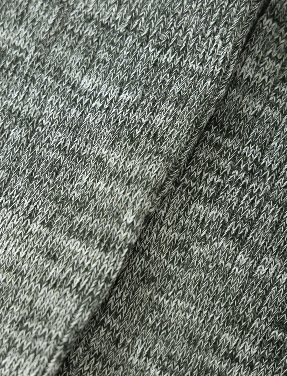 Close-up of a heathered knit fabric in mixed gray and off-white tones, showing the texture and stitch pattern with a fold running diagonally through the center.