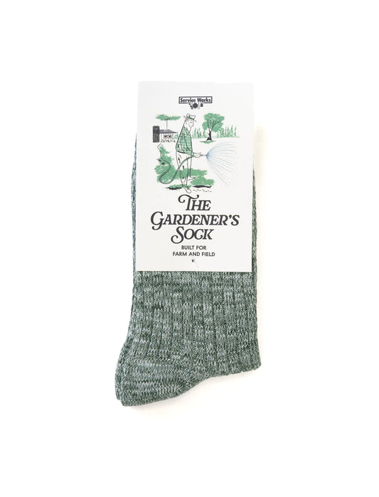 A single heathered sage green sock with a white paper label that reads 'The Gardener's Sock' and shows a small illustration of a gardener watering plants, photographed on a clean white background.