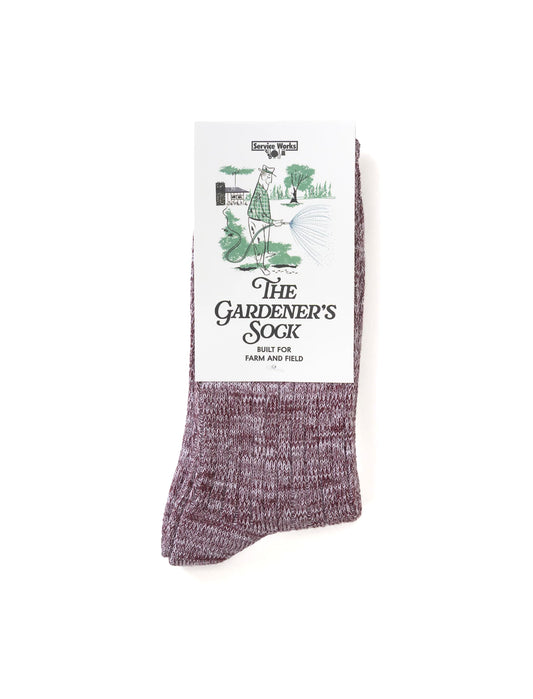 A single heathered mauve-purple sock with a white paper label that reads 'The Gardener's Sock' and shows a small garden illustration, photographed on a plain white background.