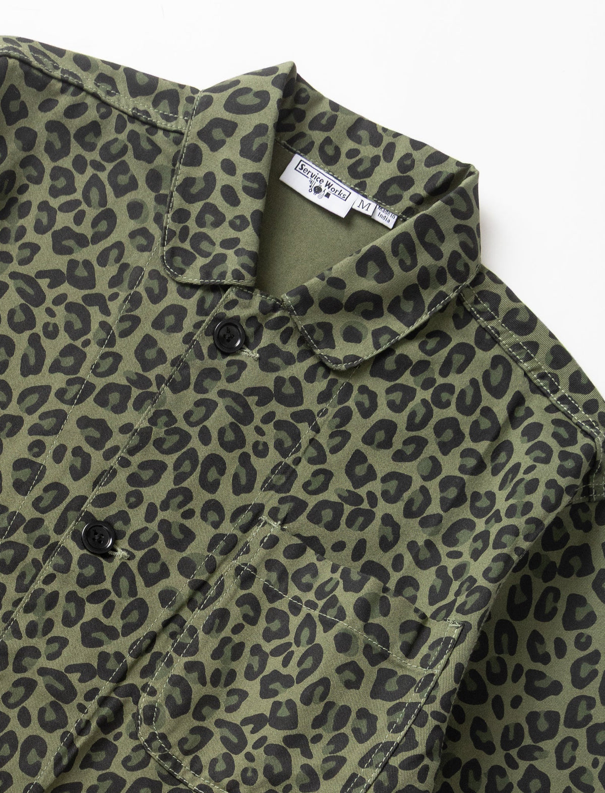 Close-up of an olive green button-up shirt with a black leopard print pattern, featuring a pointed collar and a visible neck label.