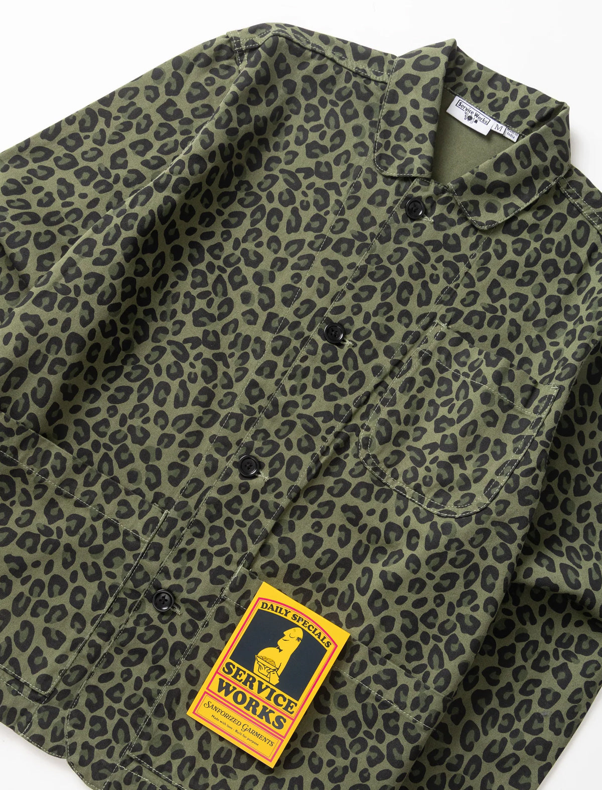 An olive green and black leopard print button-up shirt by Service Works, shown in a flat-lay view with the brand's yellow patch label visible.