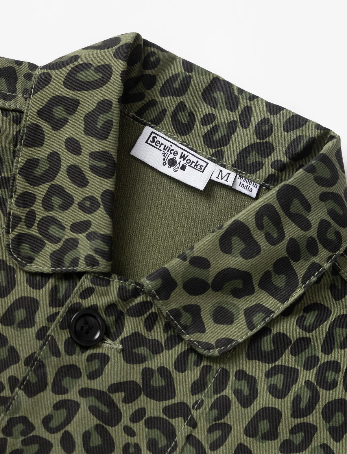 Close-up of an olive green button-up shirt with a black leopard print pattern, featuring a visible 'Service Workers' brand label on the collar.