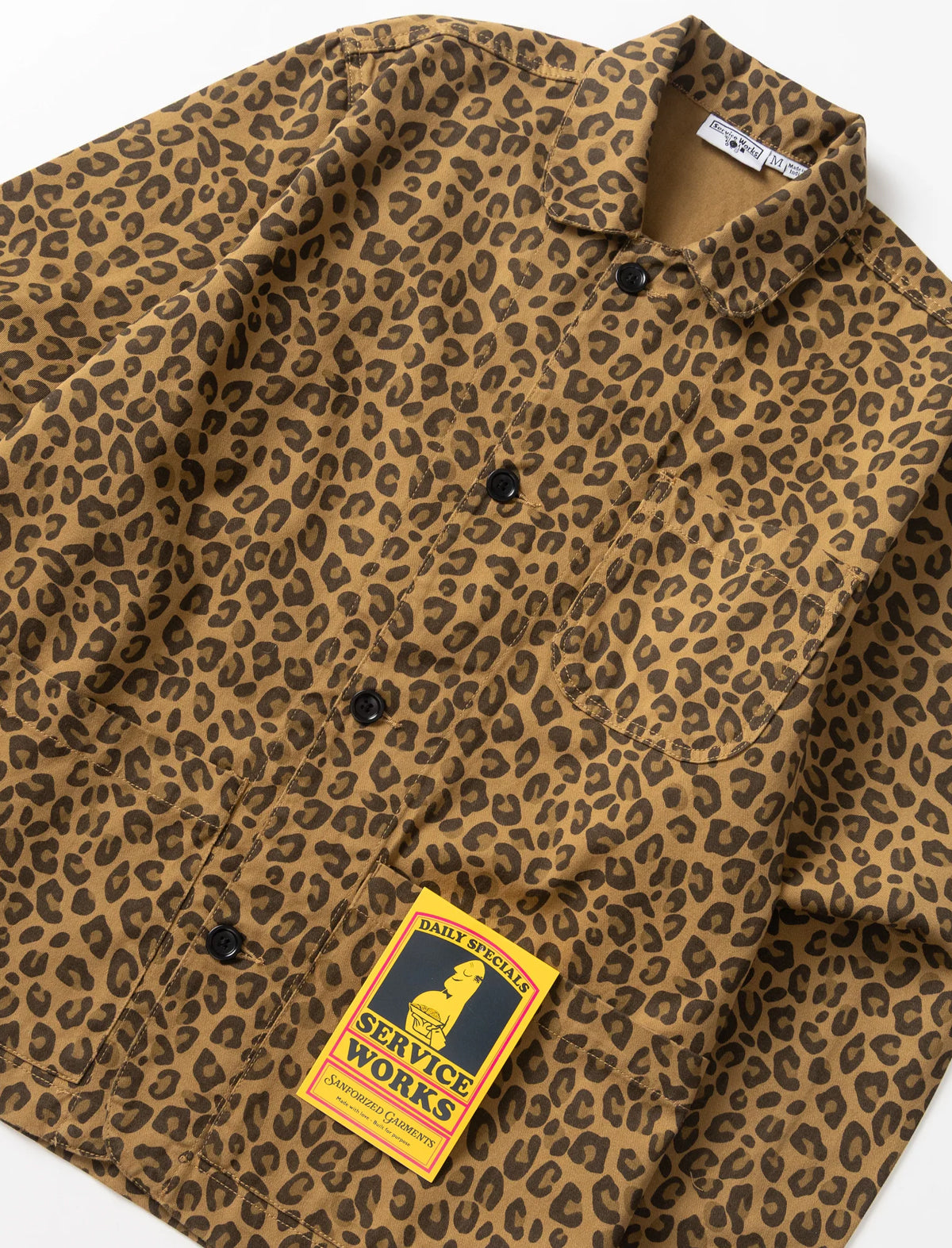A close-up of a brown and tan leopard-print button-up shirt jacket with a yellow and black Service Works patch on the chest pocket.