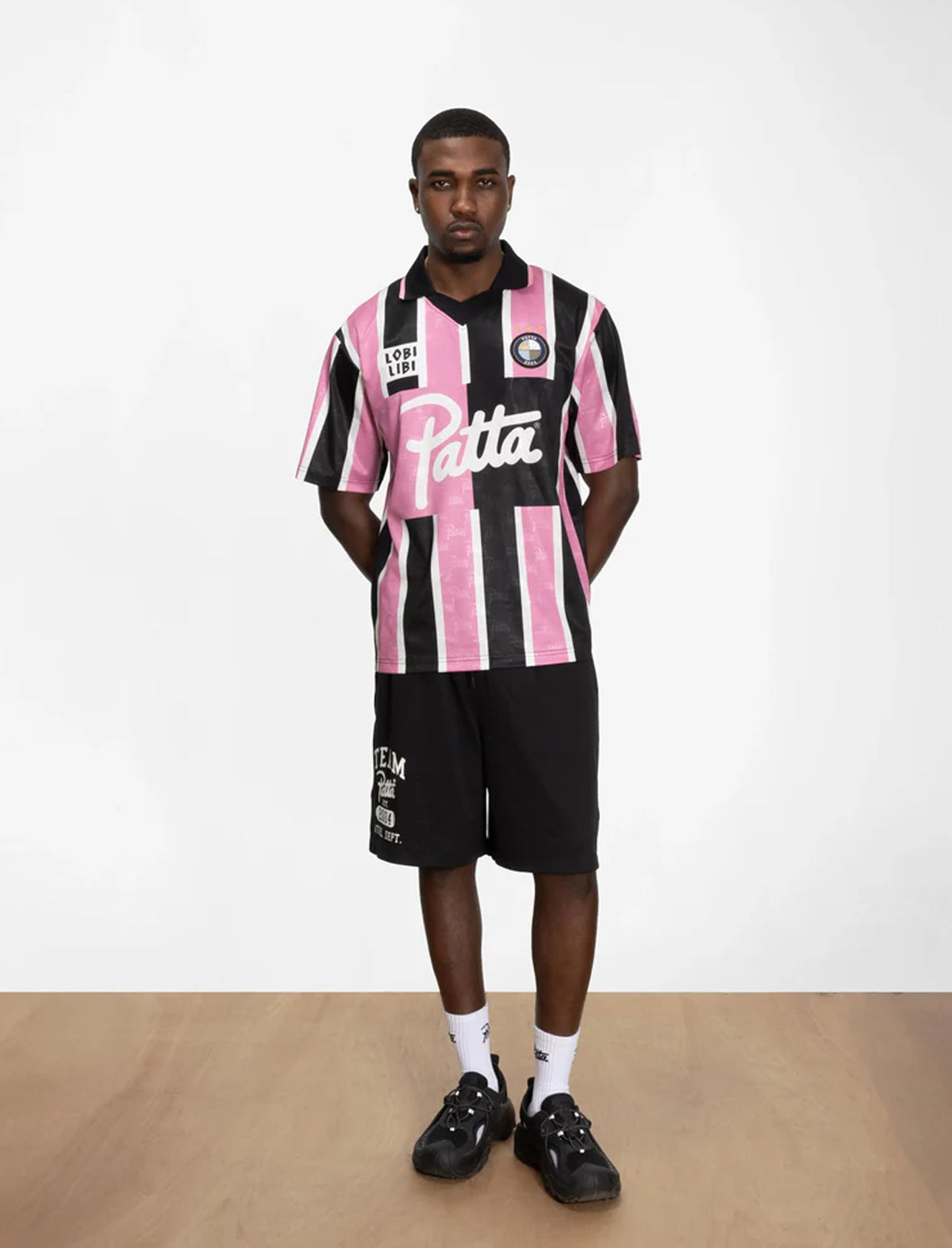 Person wearing a black and pink striped shirt with 'Patta' branding on a white background