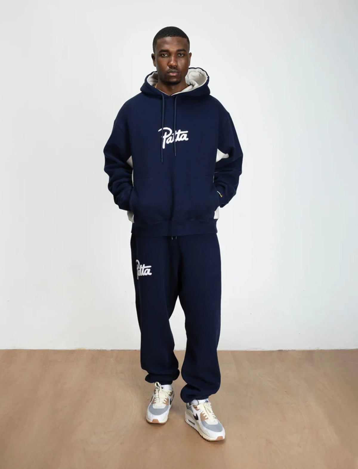 Person wearing a navy blue hoodie and pants with 'Patta' branding against a white background
