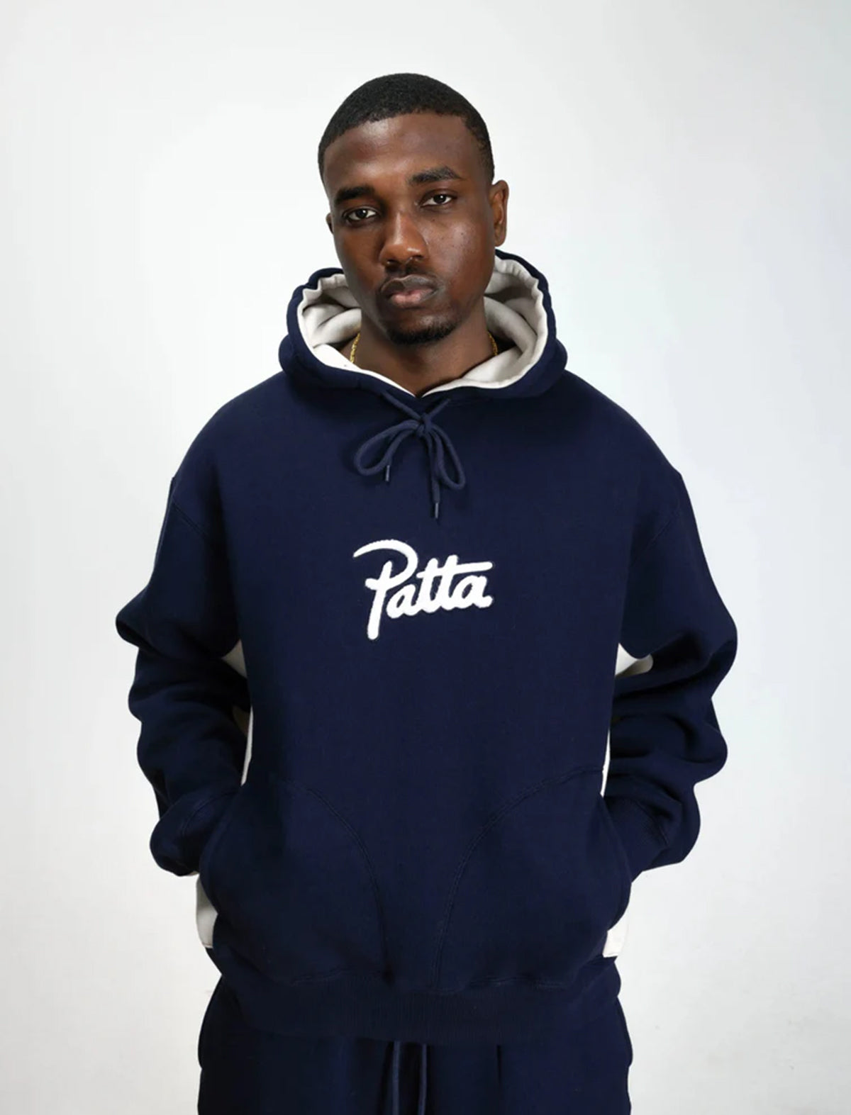 Man wearing a navy blue hoodie with 'Patta' logo on a white background