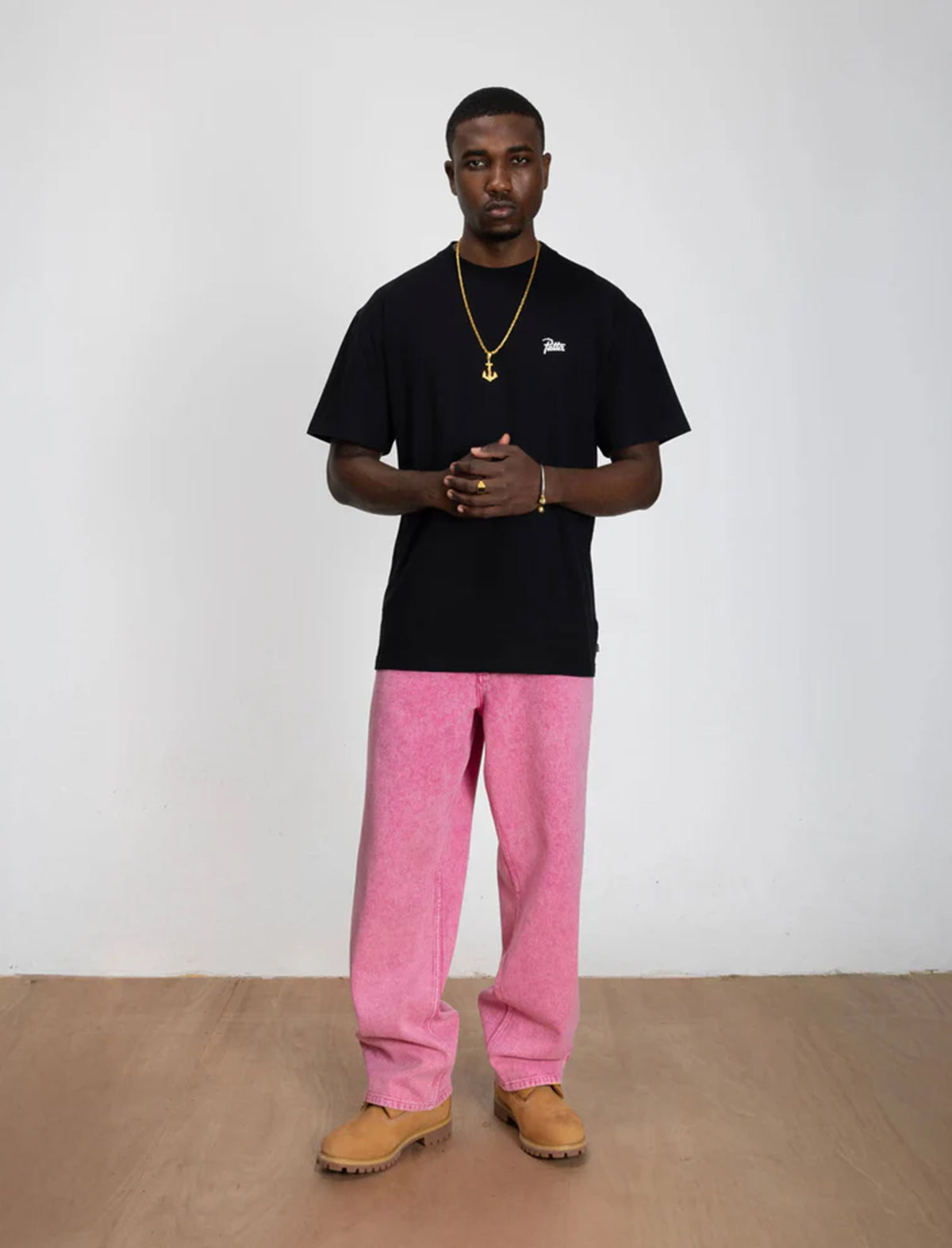 Person wearing a black Patta t-shirt and pink pants standing against a white wall.