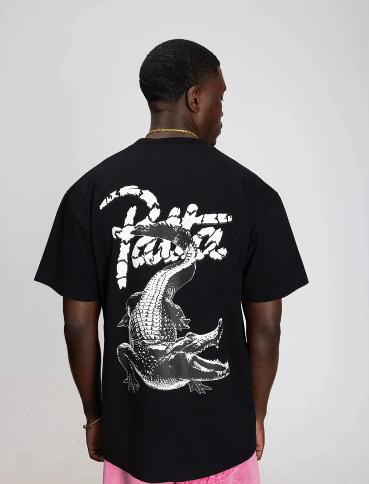 Person wearing a black Patta Croco t-shirt with a white graphic design on the back against a plain background