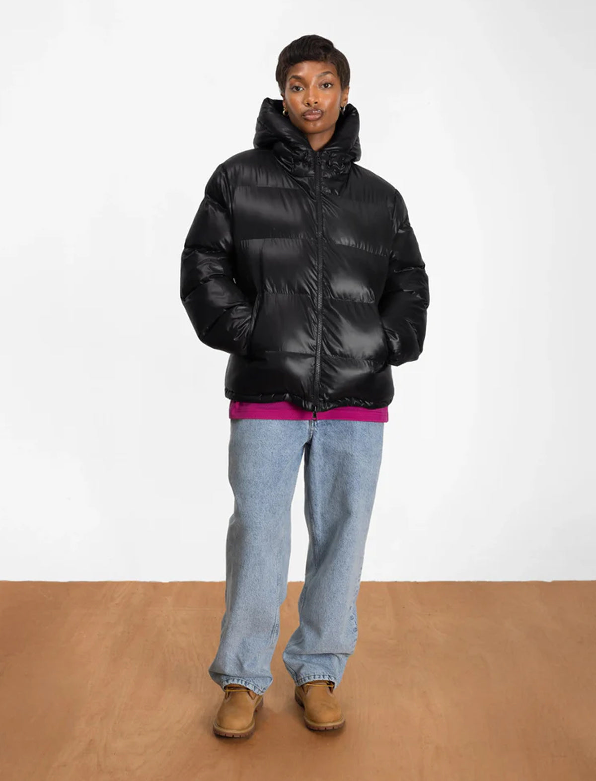Person wearing a black Patta puffer jacket, blue jeans, and brown shoes on a white background