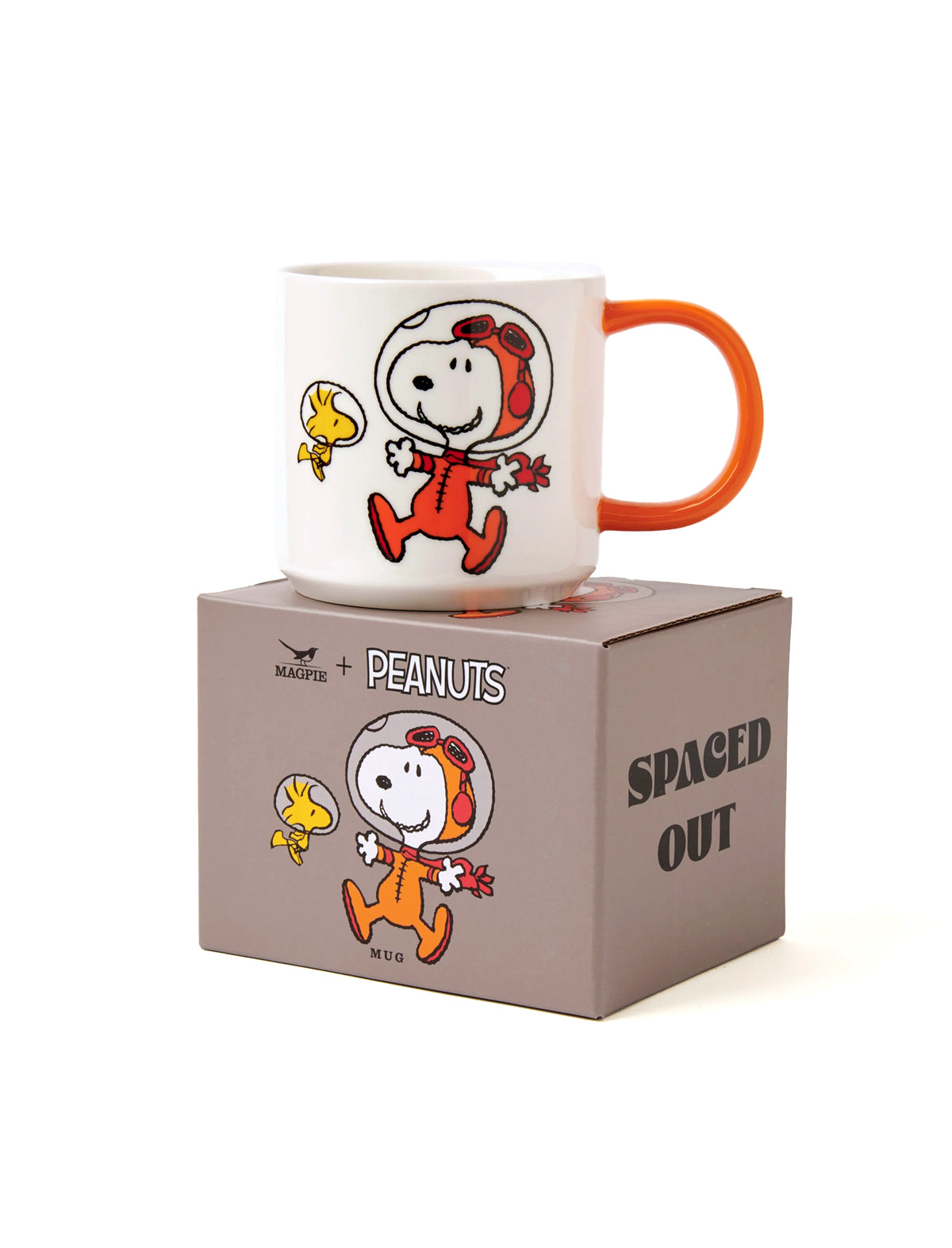 A white ceramic mug with an orange handle and printed Peanuts Snoopy and Woodstock characters artwork sits on top of its brown packaging box. The box features the text 'PEANUTS' and 'SPACED OUT'.