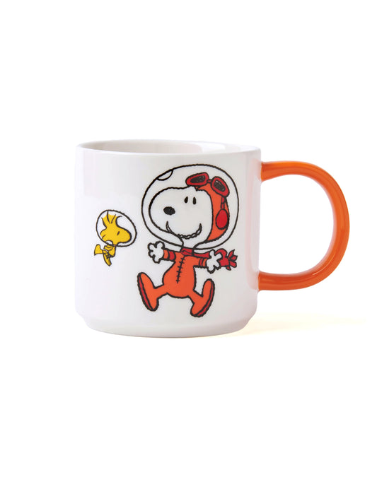 A white ceramic coffee mug featuring a printed graphic of Snoopy as an astronaut in an orange jumpsuit and Woodstock, with a bright orange handle.