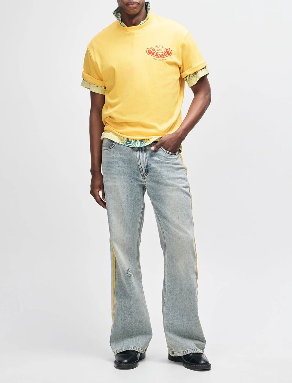 Person wearing a yellow t-shirt with a logo and light blue jeans on a white background