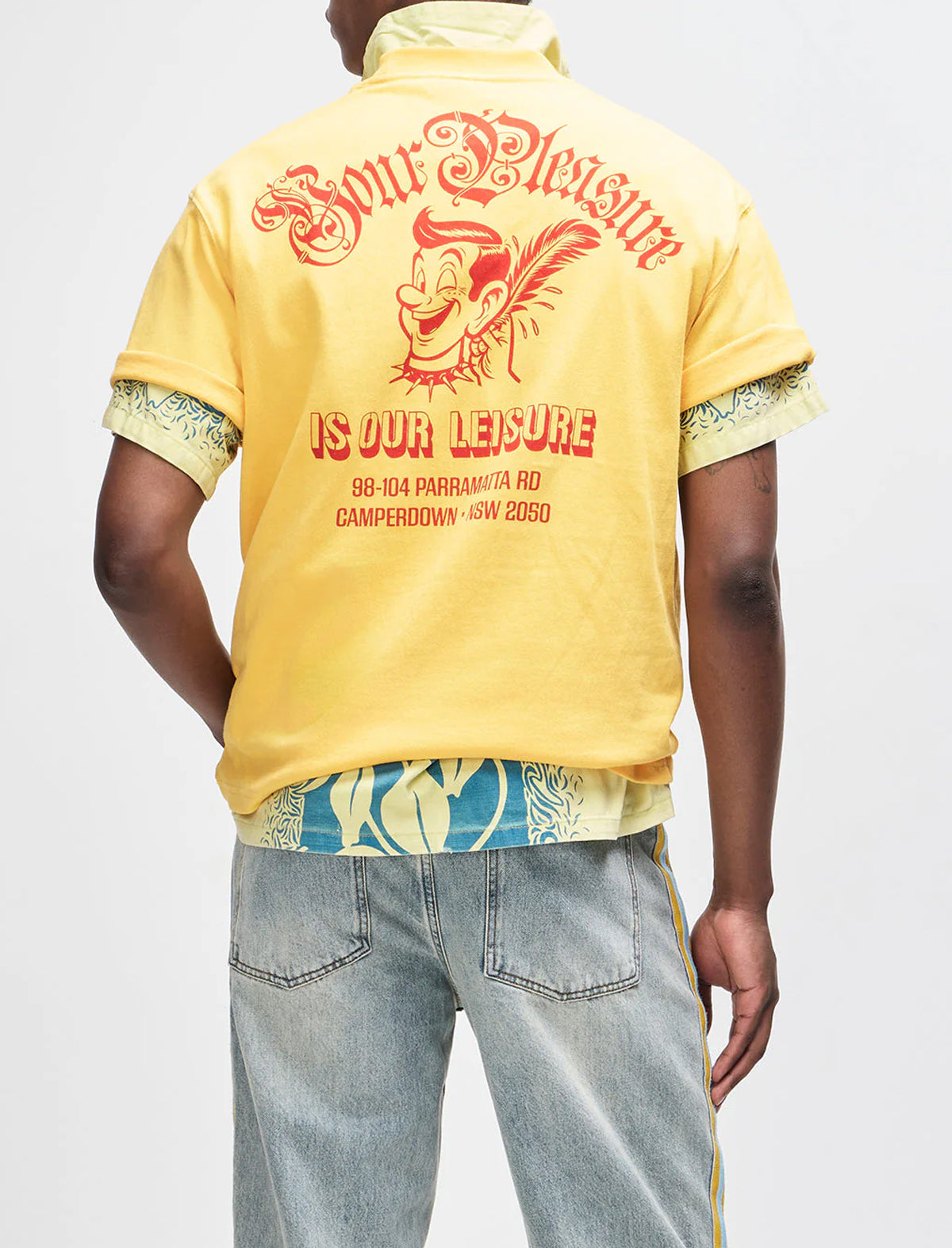 Person wearing a yellow shirt with text and graphics on the back, standing against a plain background.