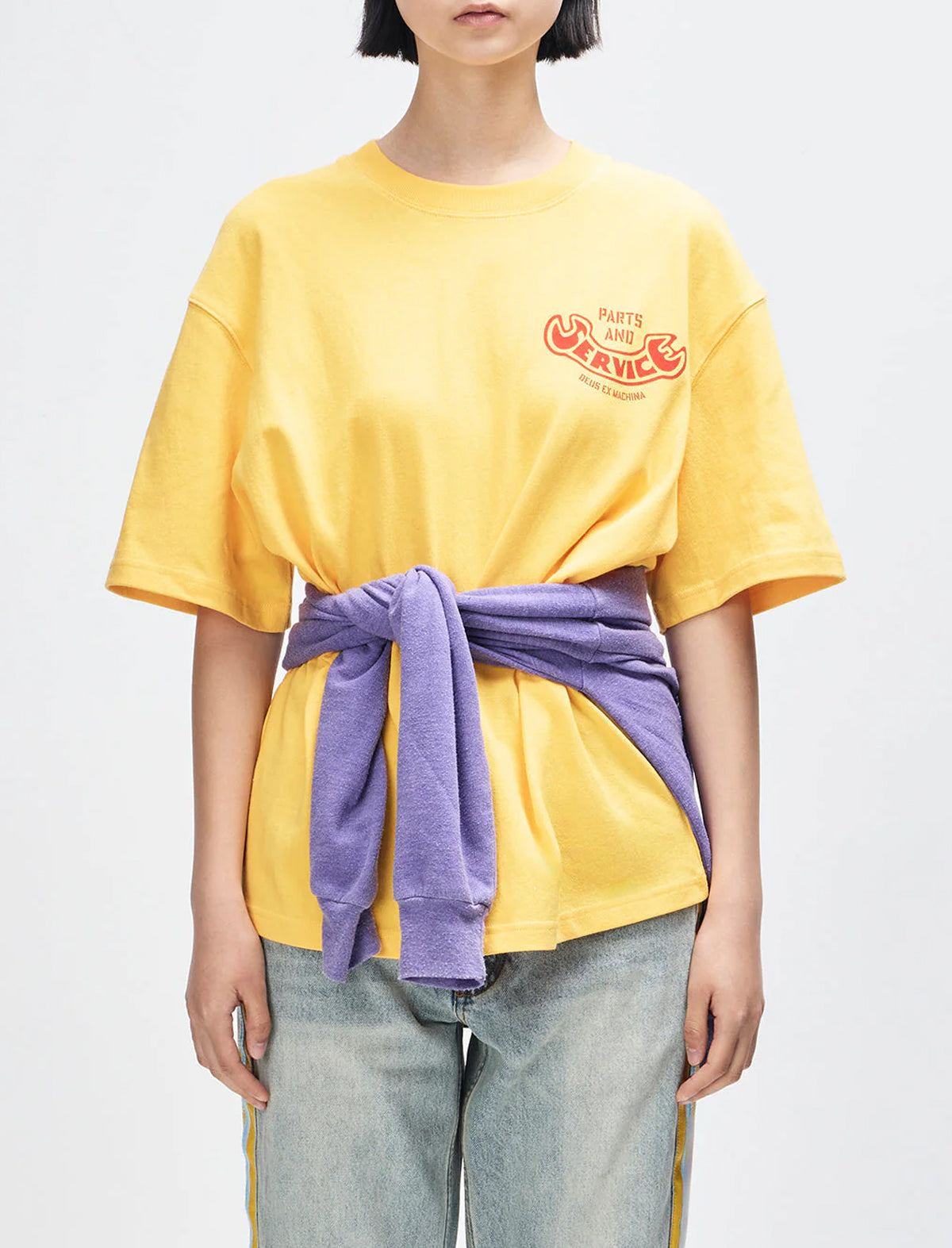Person wearing a yellow t-shirt with a logo and a purple towel tied around their waist on a white background