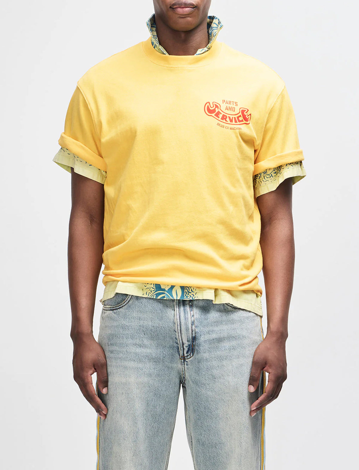 Person wearing a yellow t-shirt with graphic design and light blue jeans on a white background