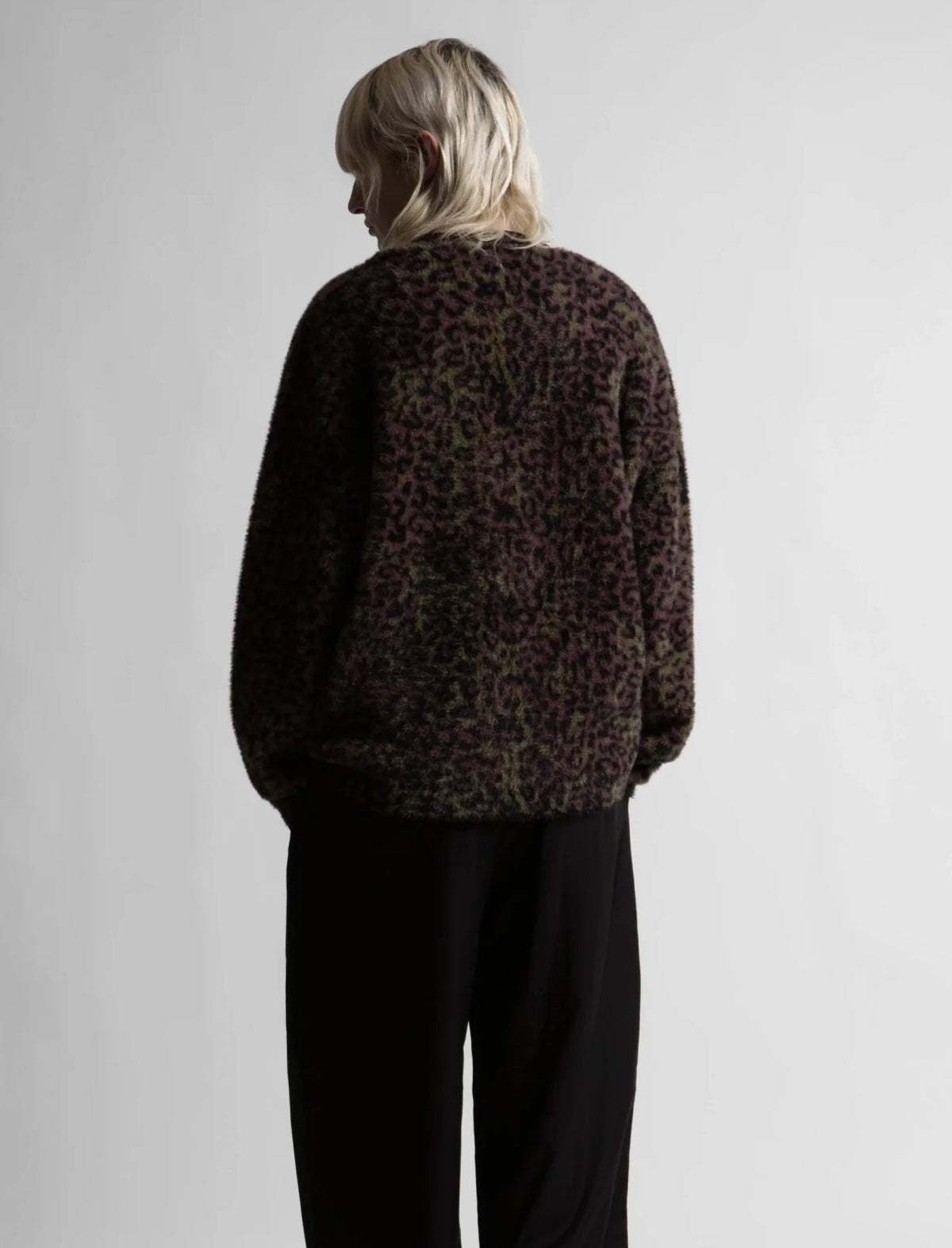 Person wearing a leopard print sweater and black pants on a plain background