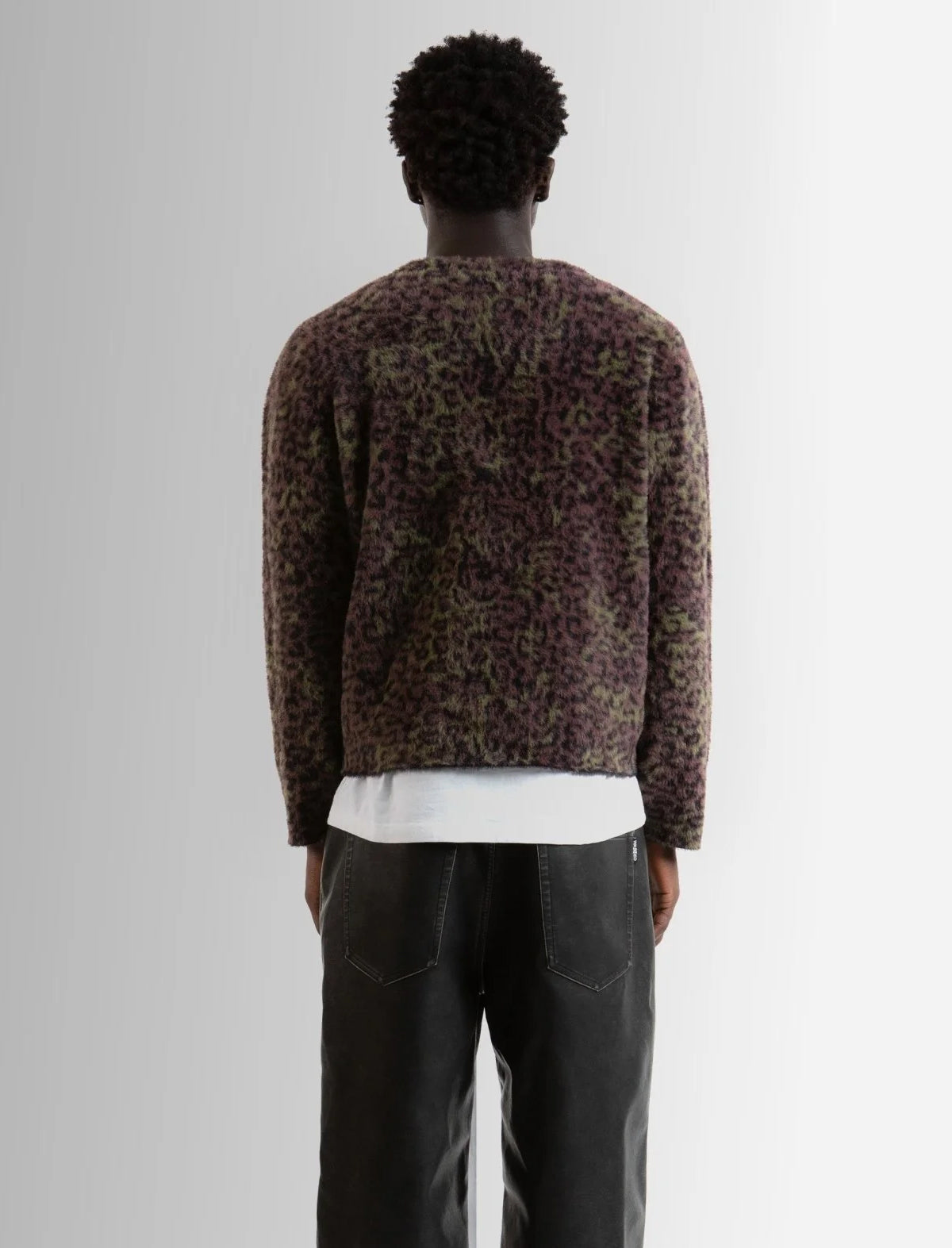 Person wearing a patterned sweater and dark pants on a plain background