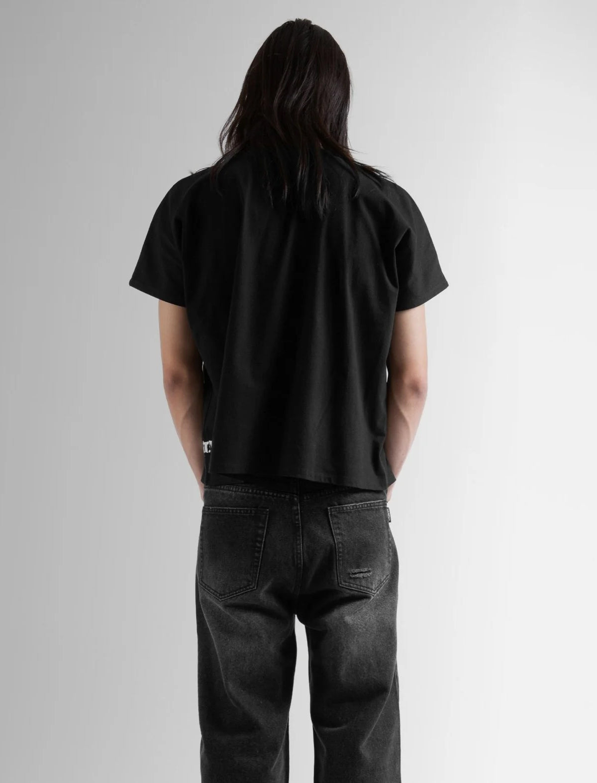 Person wearing a black t-shirt and dark jeans against a plain background