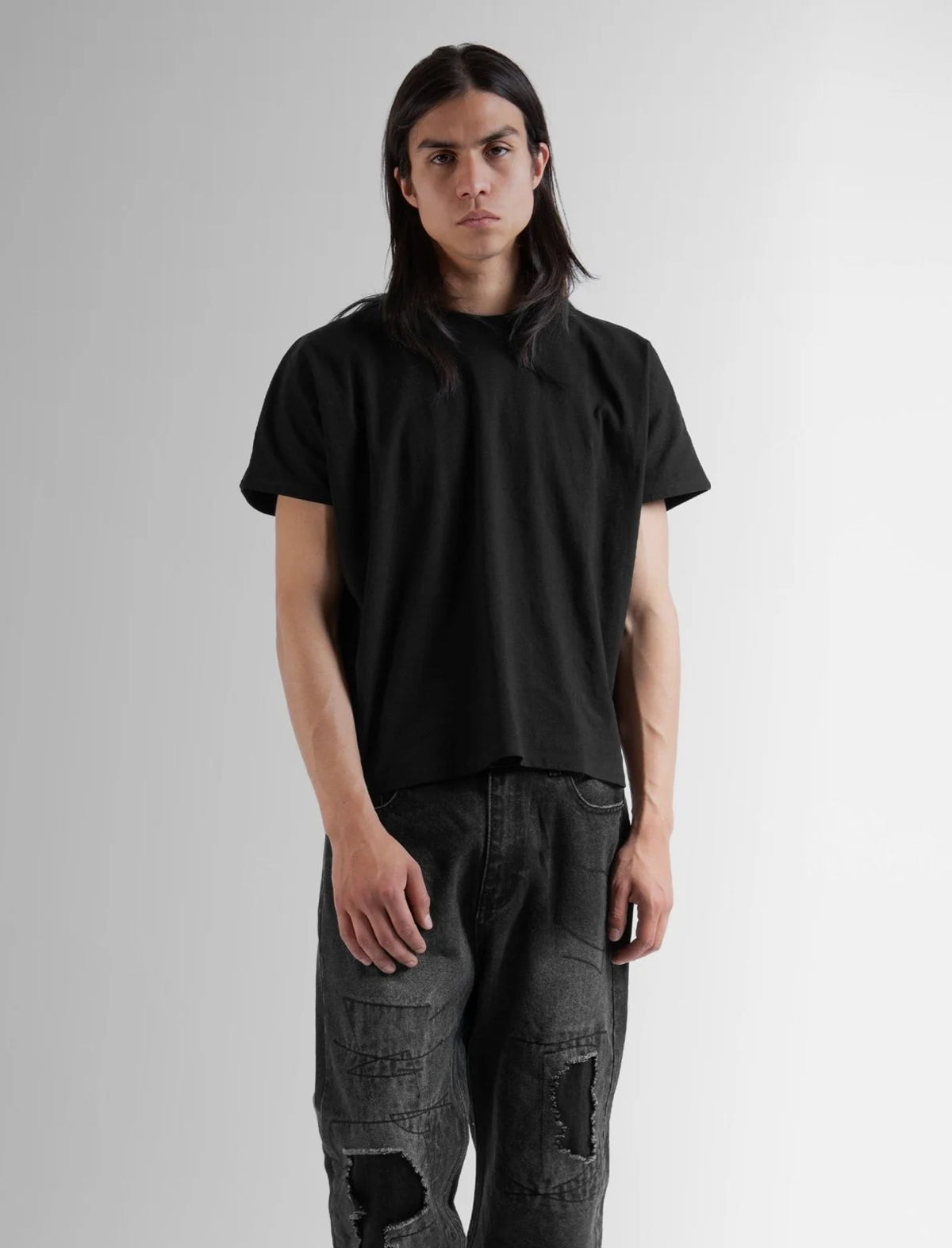 Person wearing a black t-shirt and gray jeans on a plain background