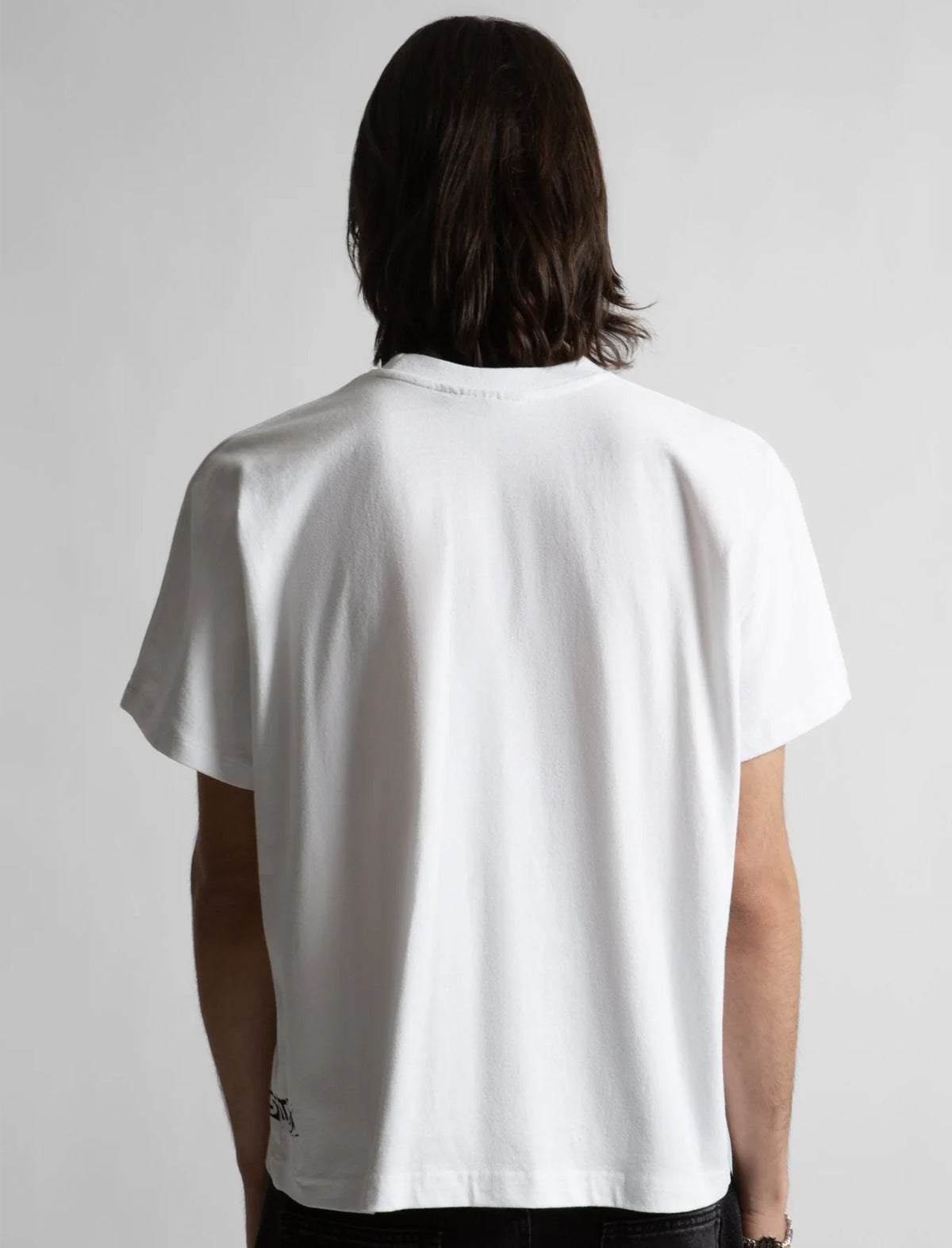 Person wearing a white t-shirt with a small logo on the back against a plain background