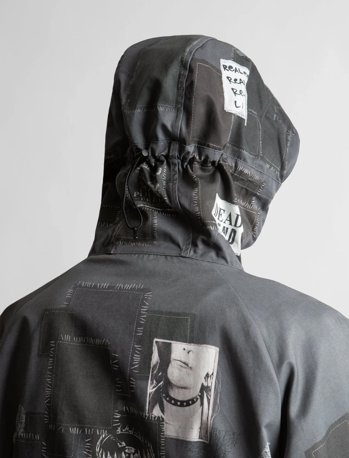 Black hooded jacket with patches and a graphic on the back against a gray background