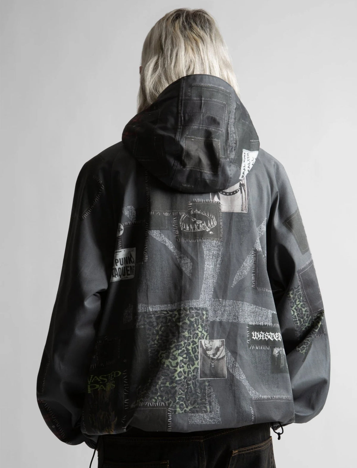 Person wearing a black and gray jacket with patches on a plain background