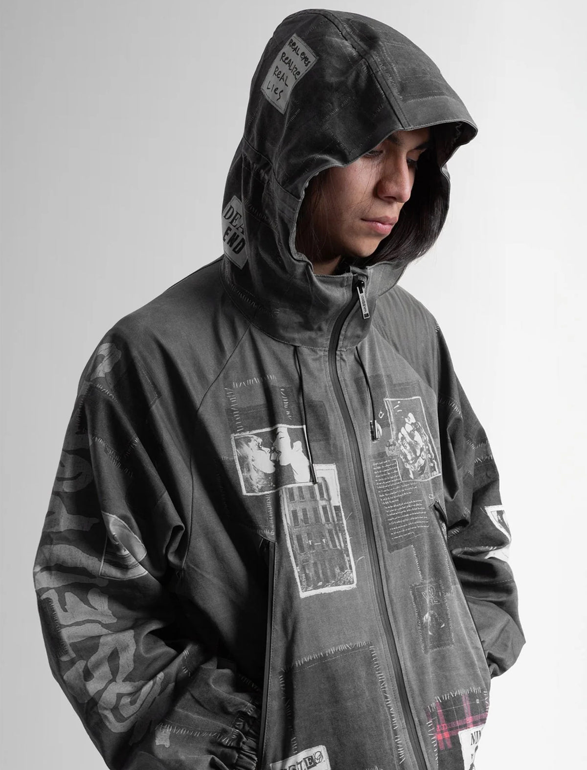Person wearing a gray hooded jacket with graphic designs on a plain background