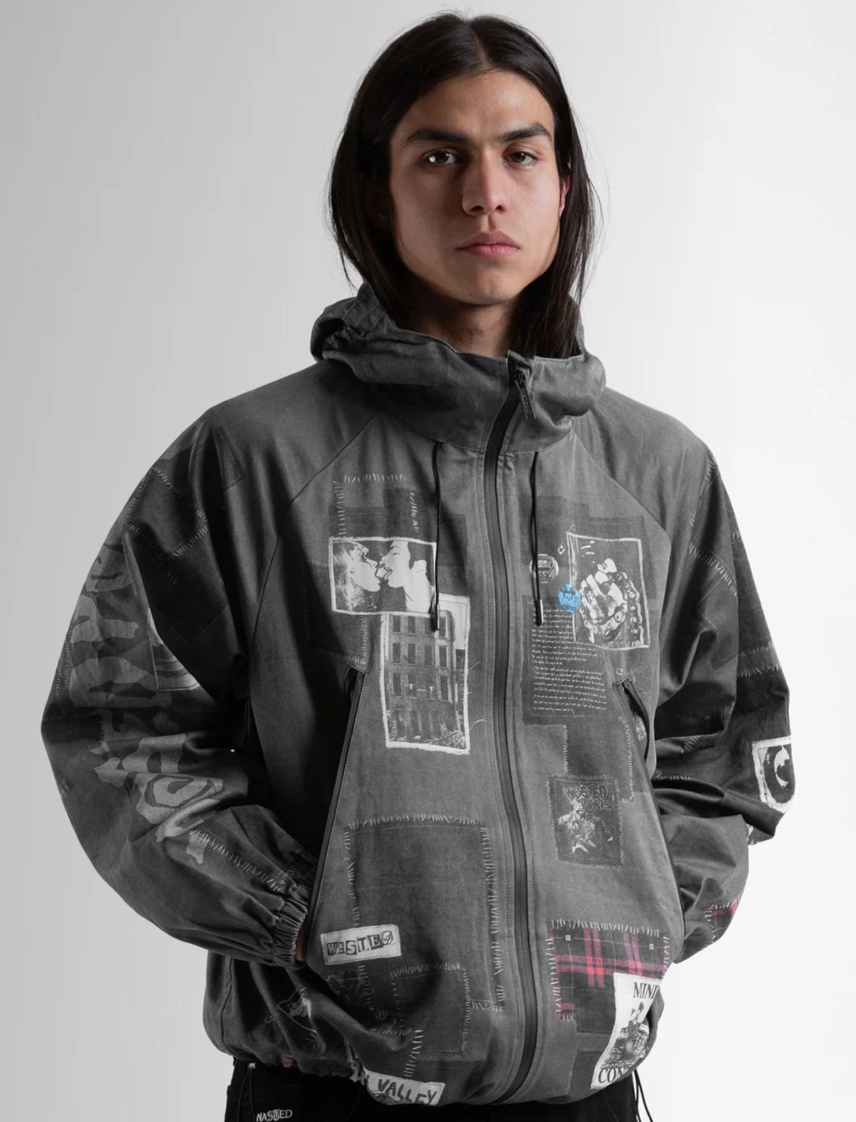 Person wearing a gray jacket with patches on a plain background
