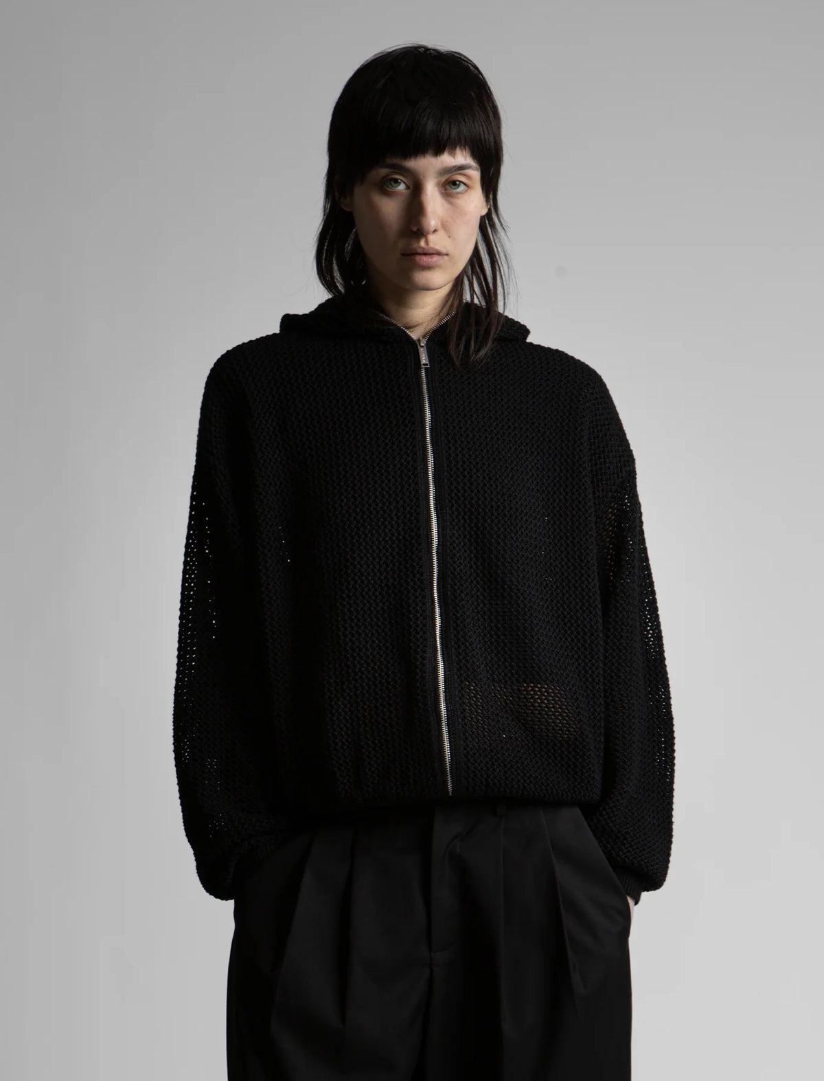 Person wearing a black zip-up hoodie against a gray background
