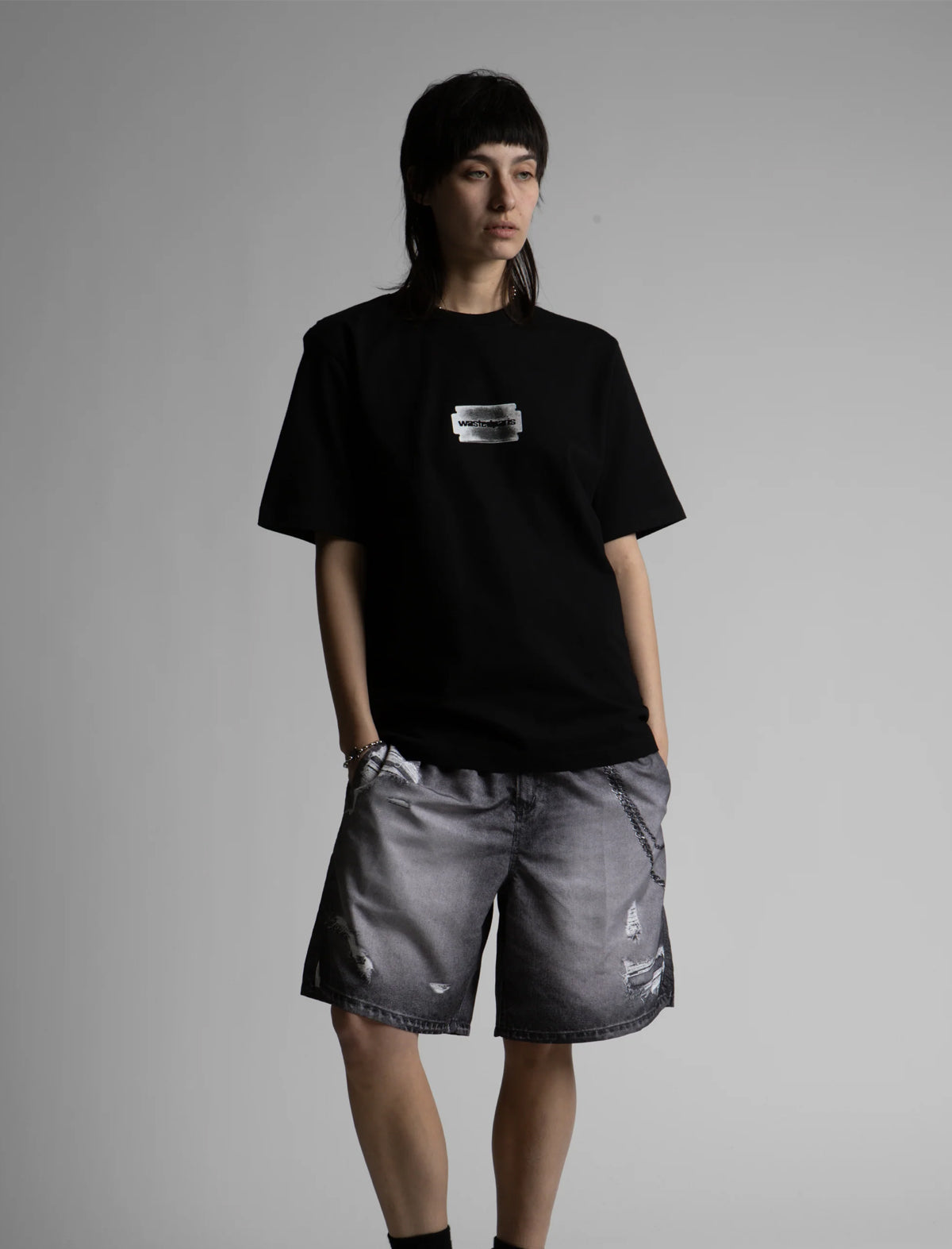 Person wearing a black t-shirt with a logo and gray shorts on a gray background