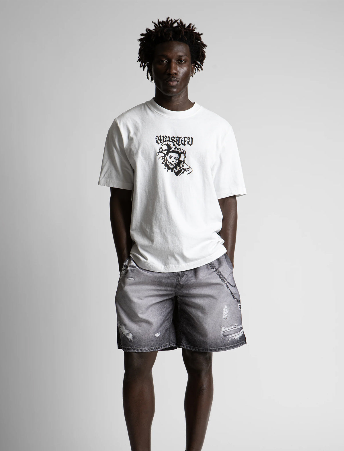 Person wearing a white t-shirt with a graphic design and gray shorts on a plain background