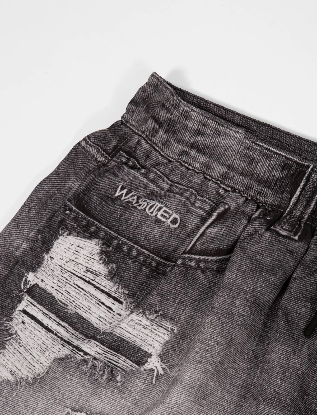 Close-up of a distressed denim jacket with 'Wasted' branding on a light gray background
