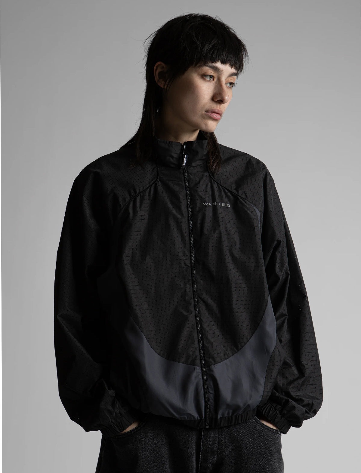 Person wearing a black jacket with a brand logo on a gray background