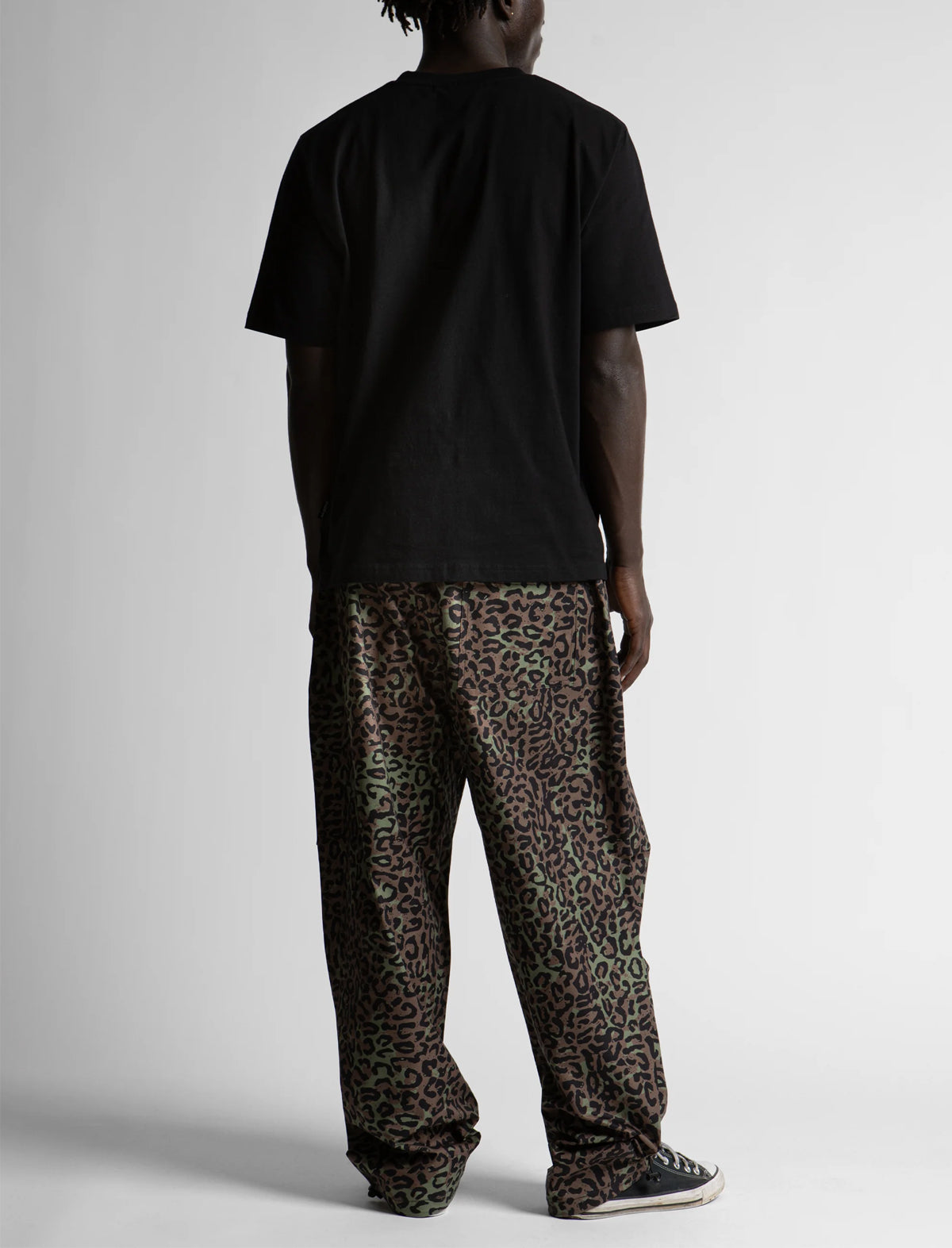 Person wearing a black t-shirt and leopard print pants on a white background