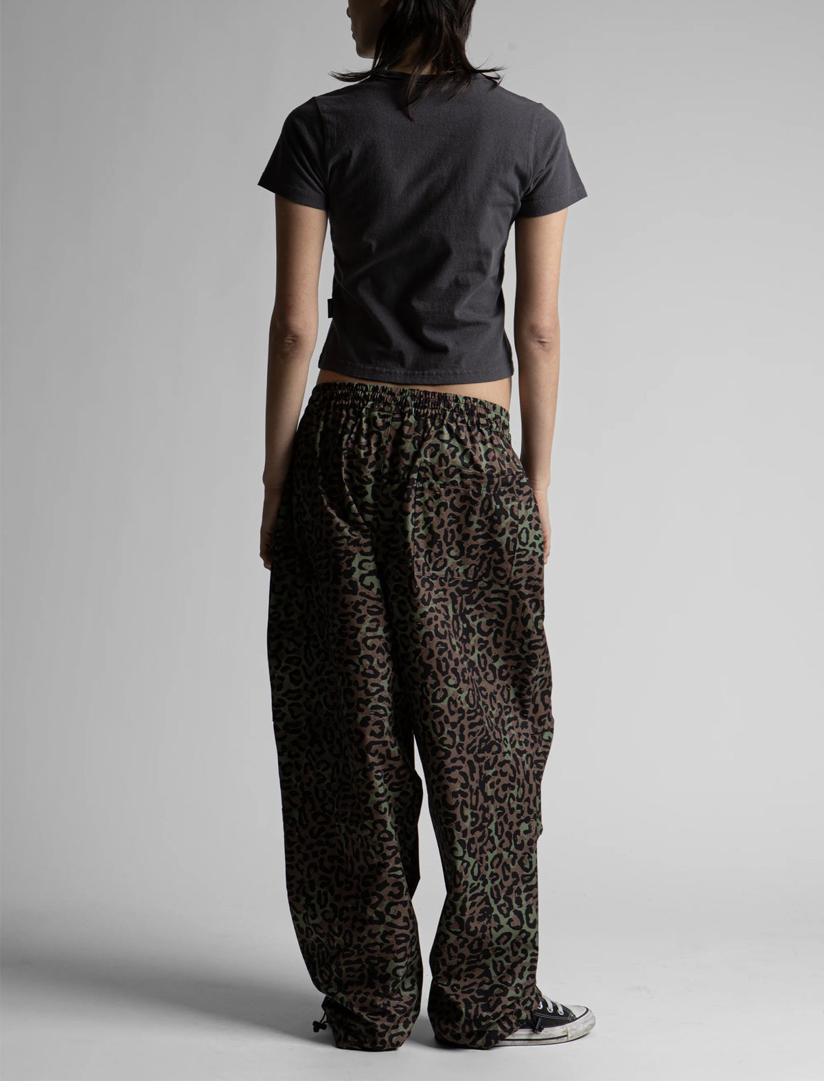 Person wearing a black t-shirt and leopard print pants on a plain background