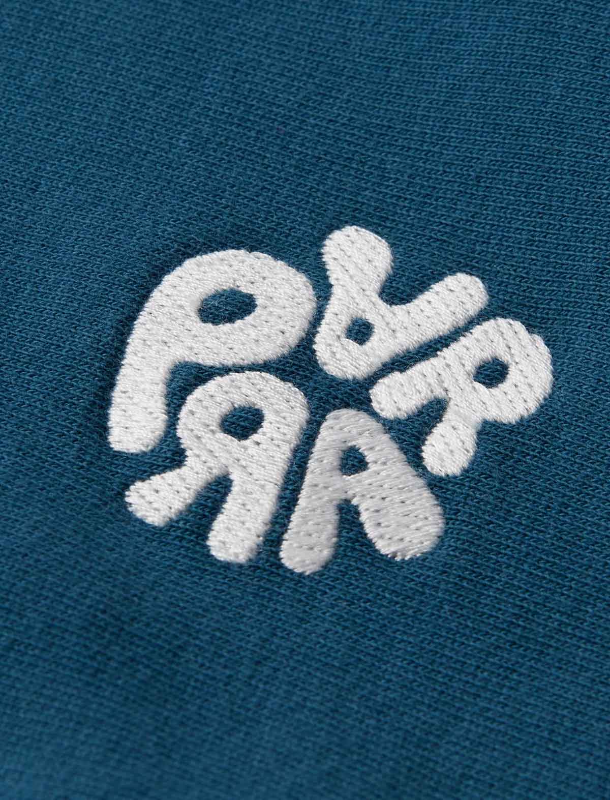 A close-up of a dark teal blue textured fabric with a stylized white embroidered logo reading 'Parra'.