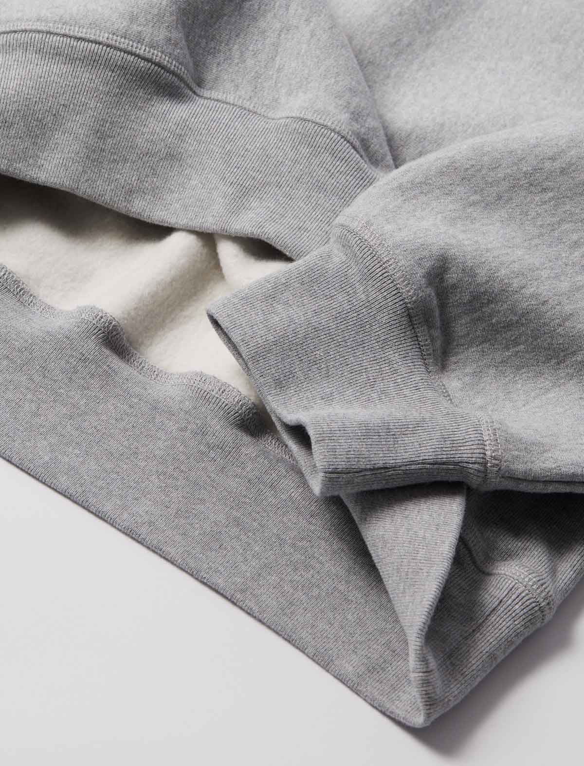 Close-up of a light gray heather sweatshirt showing the ribbed crew neck and sleeve cuffs, with a soft off-white lining visible inside.