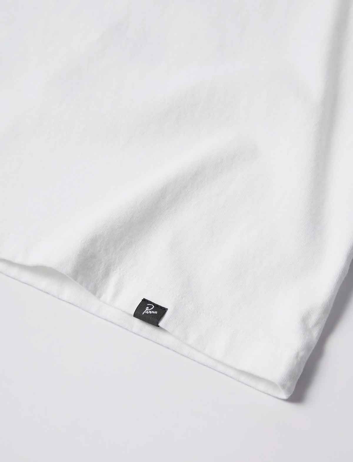 A close-up of a white fabric product, likely a t-shirt or towel, showing a folded hem with a small black brand tag featuring a white script logo.